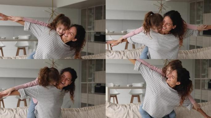 女人背着女儿像飞机翅膀一样张开双臂在室内玩耍