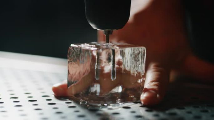 专业调酒师的特写镜头正在切割专业水晶持久冰块，为酒吧或迪斯科俱乐部的顾客准备精英酒精鸡尾酒。