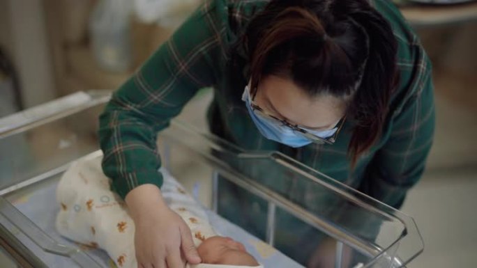 母亲戴着防病毒口罩在医院欣赏熟睡的新生儿