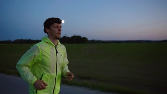 慢动作，跟踪拍摄黄昏时在高速公路上跑步的男运动员，穿着反光运动服和头灯