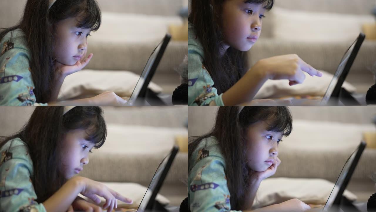 小女孩晚上在卧室玩数字平板电脑在线学习