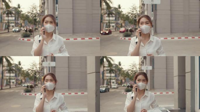 穿着时尚办公服装的成功年轻亚洲女商人在城市现代城户外独自行走时，戴着医用口罩通过手机通话。
