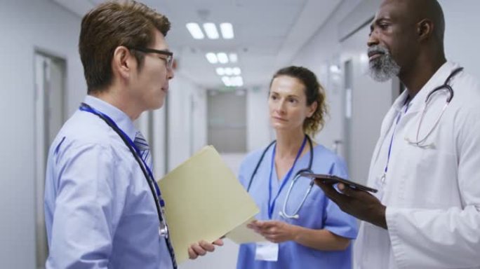 一名女性和两名男性医生在医院走廊里拿着平板电脑和文件交谈