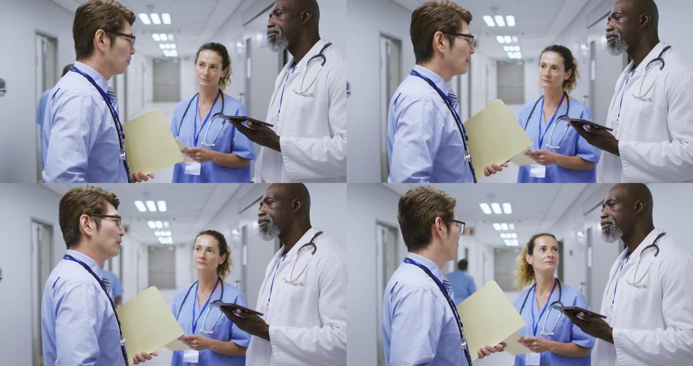 一名女性和两名男性医生在医院走廊里拿着平板电脑和文件交谈
