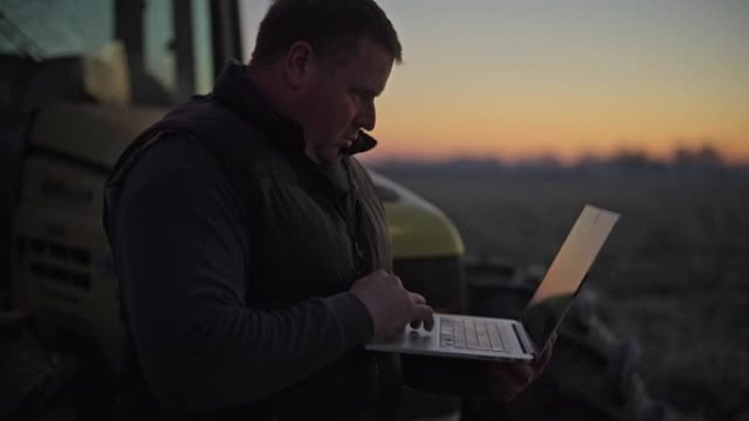 农民工作，日出时在农村地区的拖拉机上使用笔记本电脑