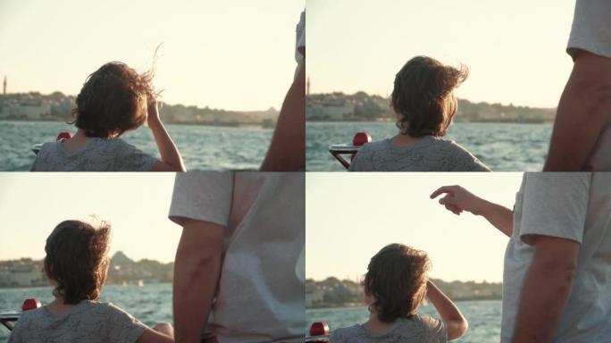 后视图快乐的十几岁男孩，风吹着头发，和爸爸在海上游轮甲板上观看令人惊叹的日落景色。