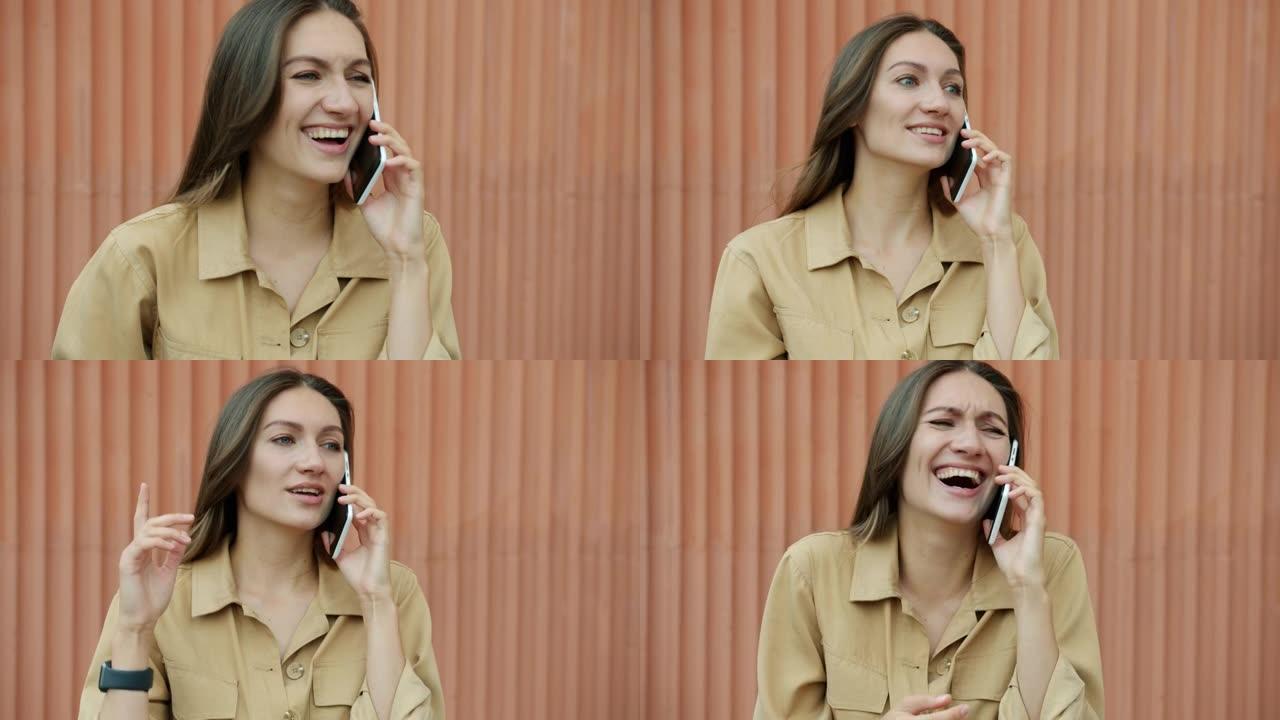 开朗的女孩正站在户外靠着城墙，在手机上笑着笑着聊天。现代技术和通信概念。