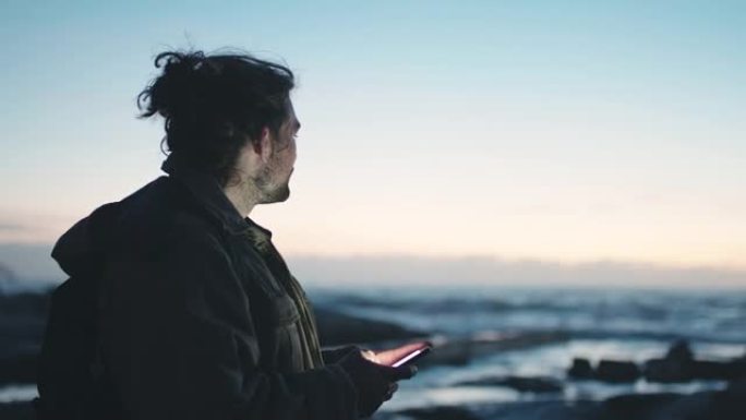 海滩，日落和man在智能手机上进行旅行博客更新，社交媒体发布并在移动应用程序上键入他在海洋的经历。海