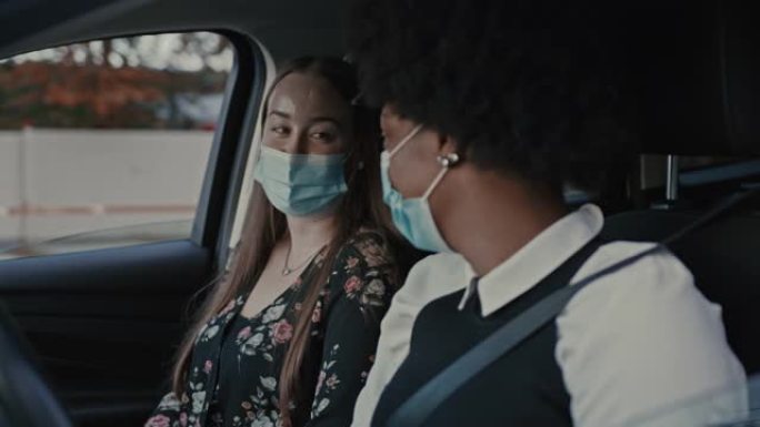 两名年轻女性在汽车上交谈并戴着保护性医用口罩