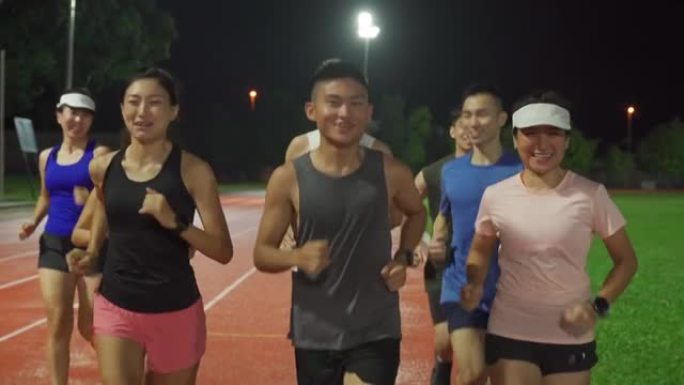 前视图亚洲中国运动员队在夜间下雨天气中在田径体育场上跑步