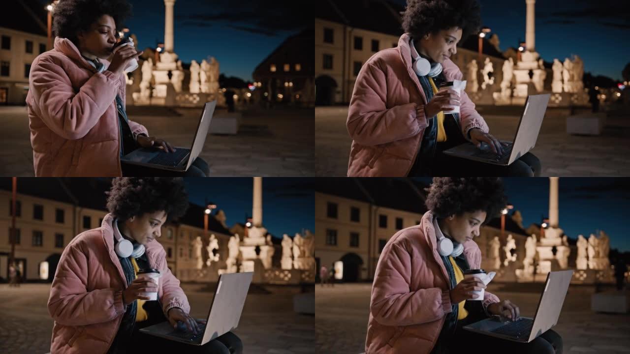 年轻女子坐在城市的长凳上，一边用笔记本电脑工作，一边喝咖啡