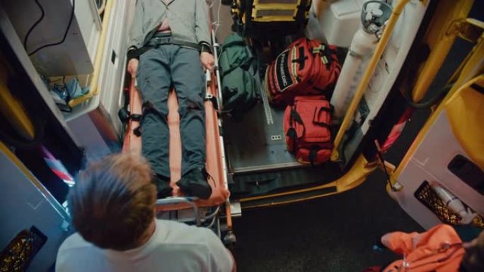 一组EMS医护人员将受伤的病人送往医院，并用担架将他从救护车中救出的镜头。紧急护理助理帮助年轻人在事