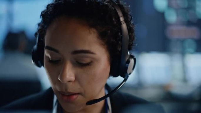 专业IT技术支持女性专家的肖像在数字屏幕监控控制室的计算机上工作。员工戴着带麦克风的耳机，正在通话。