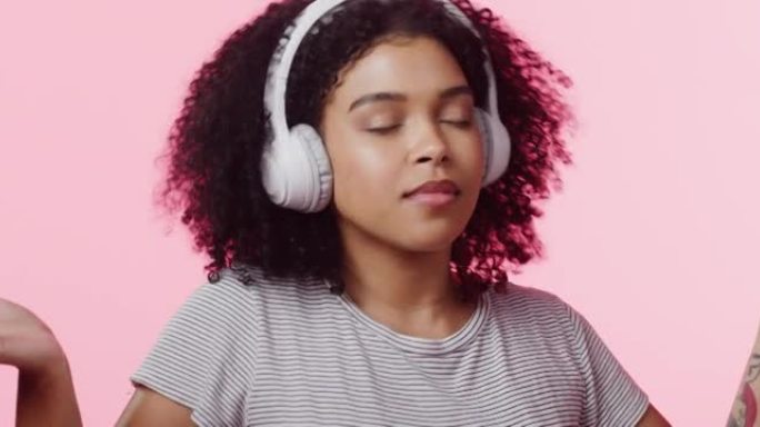 4k视频片段，一个美丽的年轻女子戴着耳机在粉红色背景下跳舞和唱歌