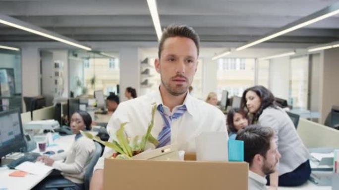 4k视频片段，一位英俊的年轻商人在被解雇后背着一箱他的物品穿过办公室