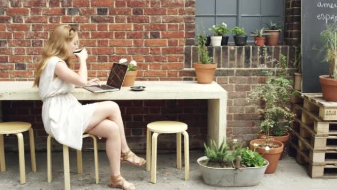 4k视频片段，一个迷人的年轻女子独自坐在咖啡馆外并使用笔记本电脑