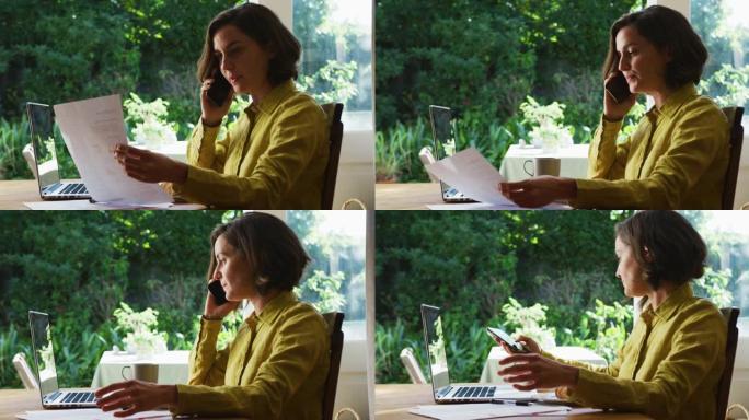 白人妇女的中段使用在家工作的笔记本电脑在智能手机上聊天