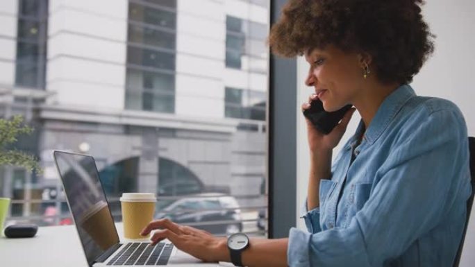 现代办公室的女商人在笔记本电脑上工作并接听手机