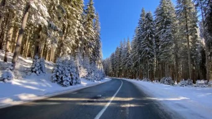 在阳光明媚的日子里，冬天在积雪覆盖的森林的空旷道路上行驶