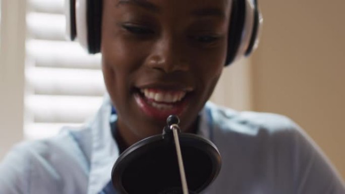 在家中戴着耳机的非裔美国妇女在麦克风中唱歌