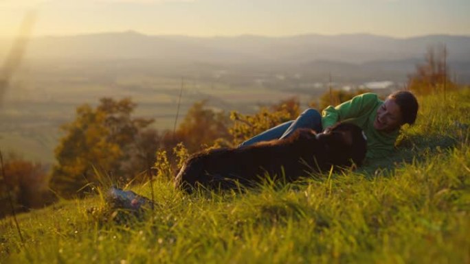 日落时，SLO MO女人在山上的草地上与狗一起玩很有趣