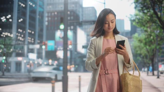 一位迷人的日本女性穿着时髦的休闲服，在城市街道上使用智能手机的肖像。大城市的经理与人们在线联系，消息