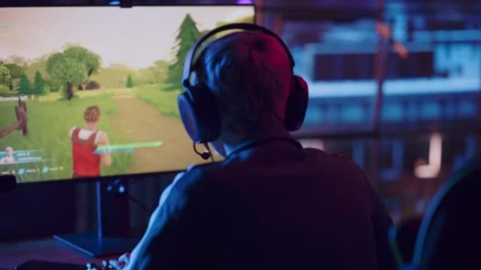 在一个年轻的女性游戏玩家的肩膀角度，戴上耳机，在家里霓虹灯照明的客厅里的个人电脑上玩视频游戏。阁楼公