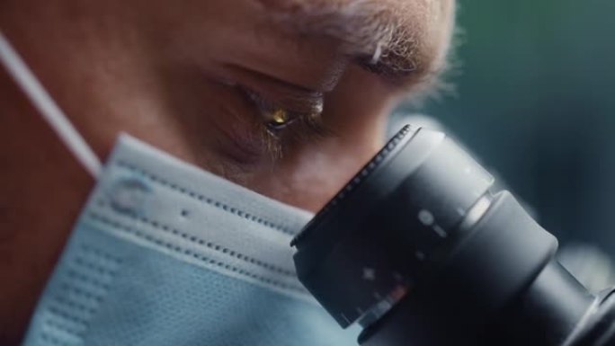 Ultra Macro特写了一名戴着医用口罩并看着显微镜的男性科学家的镜头。微生物学家使用技术设备在
