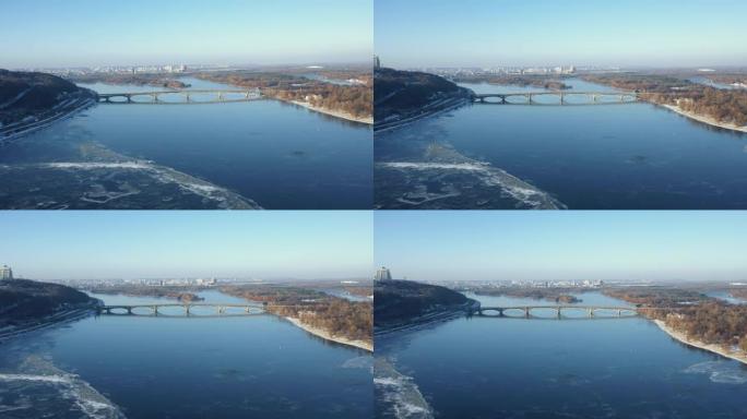 无人驾驶飞机在基辅冰冻的第聂伯河上高高飞过美丽的桥梁全景，在晴朗的冬日天空下。