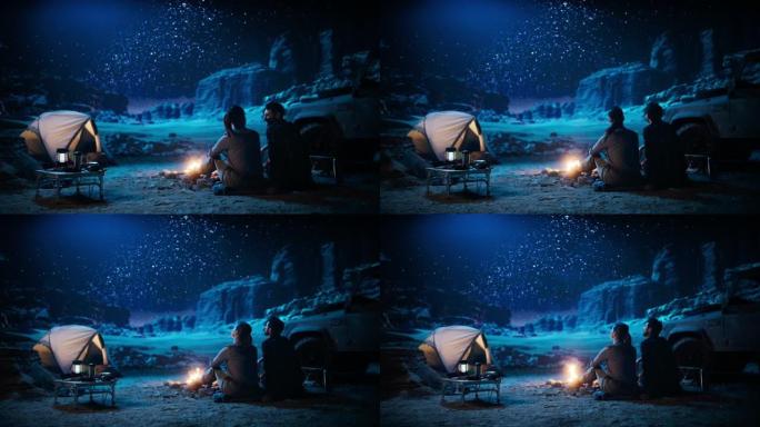 快乐的情侣帐篷在峡谷里露营，坐在篝火旁看着夜空，银河里满是明亮的星星。两个恋爱中的旅行者在浪漫的假期