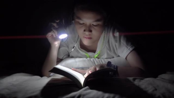 聪明的亚洲女孩在卧室里用手电筒看书