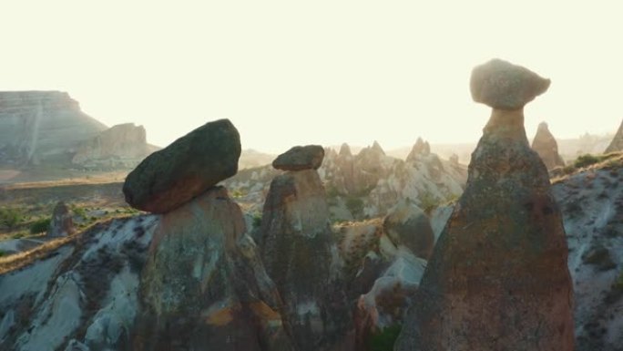 在卡帕多西亚土耳其的沙漠天空下，无人驾驶飞机在雄伟的高大岩石上摇摄，上面放着神秘的大石头。