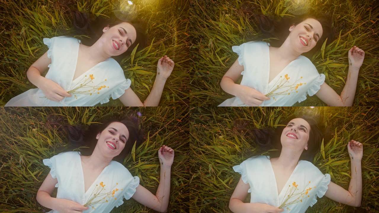 穿着白色连衣裙躺在草地上的SLO MO快乐年轻女子