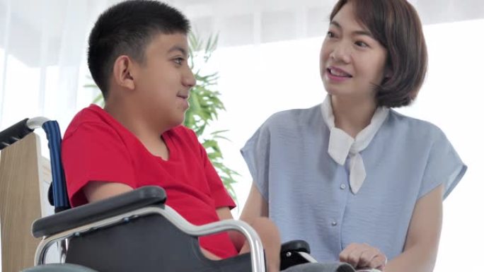 坐在轮椅上的亚洲青少年残疾男孩在家中与亚洲年轻女性护理员交谈感到高兴。
