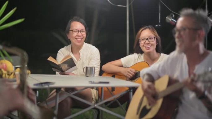 亚洲华裔妻子看着丈夫弹吉他家人和朋友喜欢玩乐器花园派对聚会露营帐篷晚上