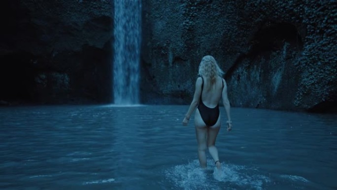 美丽的女人晚上在雨林中漫步在瀑布旁，在水中游泳，穿着泳衣享受平静的夜晚