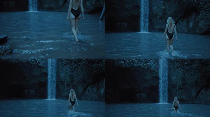 美丽的女人晚上在雨林中漫步在瀑布旁，在水中游泳，穿着泳衣享受平静的夜晚