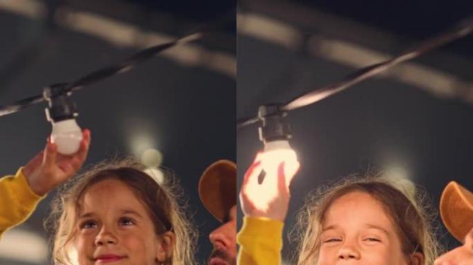 垂直屏幕: 父亲帮助他美丽的小女儿在家里的仙女灯后院安装了灯泡。父女击掌并庆祝成功修复。