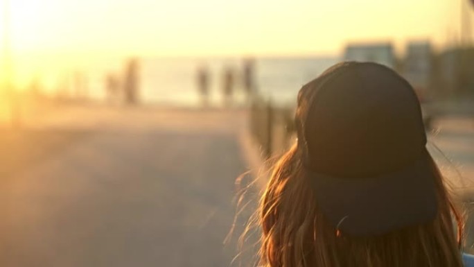 日落时，棕色头发的特写年轻女子走在海滩的木板路上，后视