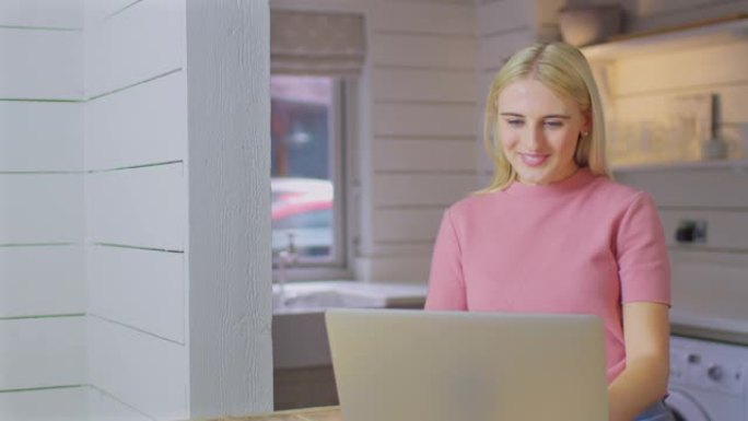 年轻女子站在家里的厨房柜台上，用笔记本电脑进行视频通话