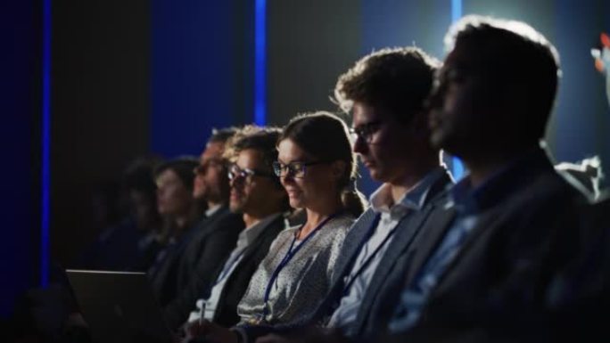 女性坐在科技会议上黑暗拥挤的礼堂里。使用笔记本电脑的年轻女子。专家观看有关新软件和高科技产品的创新技
