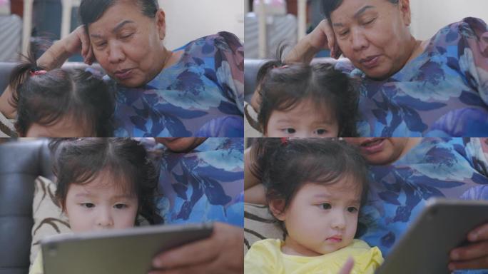 手持视点拍摄祖母在家客厅和孙子一起观看数字平板电脑。快乐的祖父母和她的孙女一起看着数字屏幕，感到在家