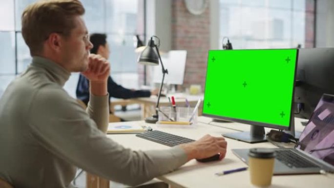 白天在现代明亮的办公室里，年轻的高加索人在笔记本电脑和绿屏电脑上工作。创意软件开发人员使用色度键显示