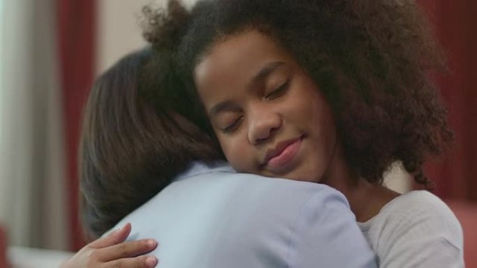一位母亲拥抱着一个黑人女儿，她在拥抱母亲的过程中幸福，温暖和安全地对着镜头微笑。