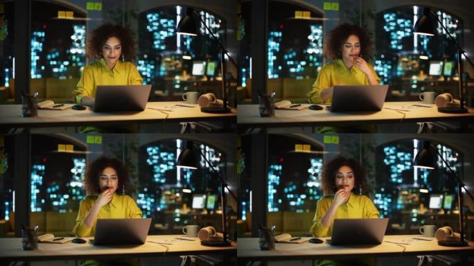 一个快乐的中东经理坐在创意办公室的办公桌前的肖像。时尚的女性，卷发，使用笔记本电脑，在夜间考虑营销机