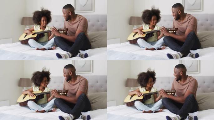 非裔美国父亲和他的女儿坐在床上一起弹吉他