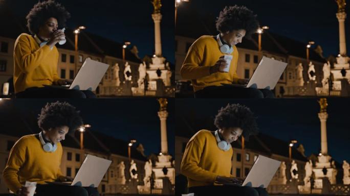快乐的年轻女子坐在城市的长凳上，一边用笔记本电脑工作，一边喝咖啡