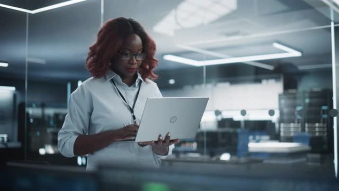 技术软件工程部门经理站立并使用笔记本电脑的肖像。非洲女性在办公室工作时望着远方思考