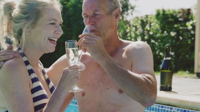 退休的高级夫妇暑假在游泳池放松庆祝喝香槟