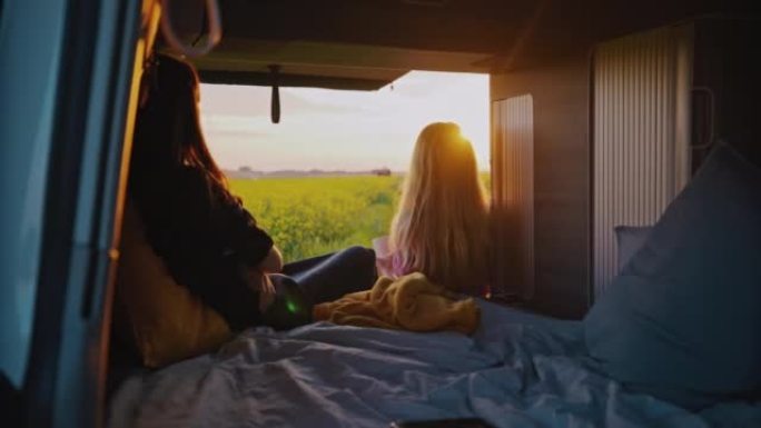 DS两名妇女喜欢面包车的生活，同时欣赏停在油菜籽田的露营车的景色